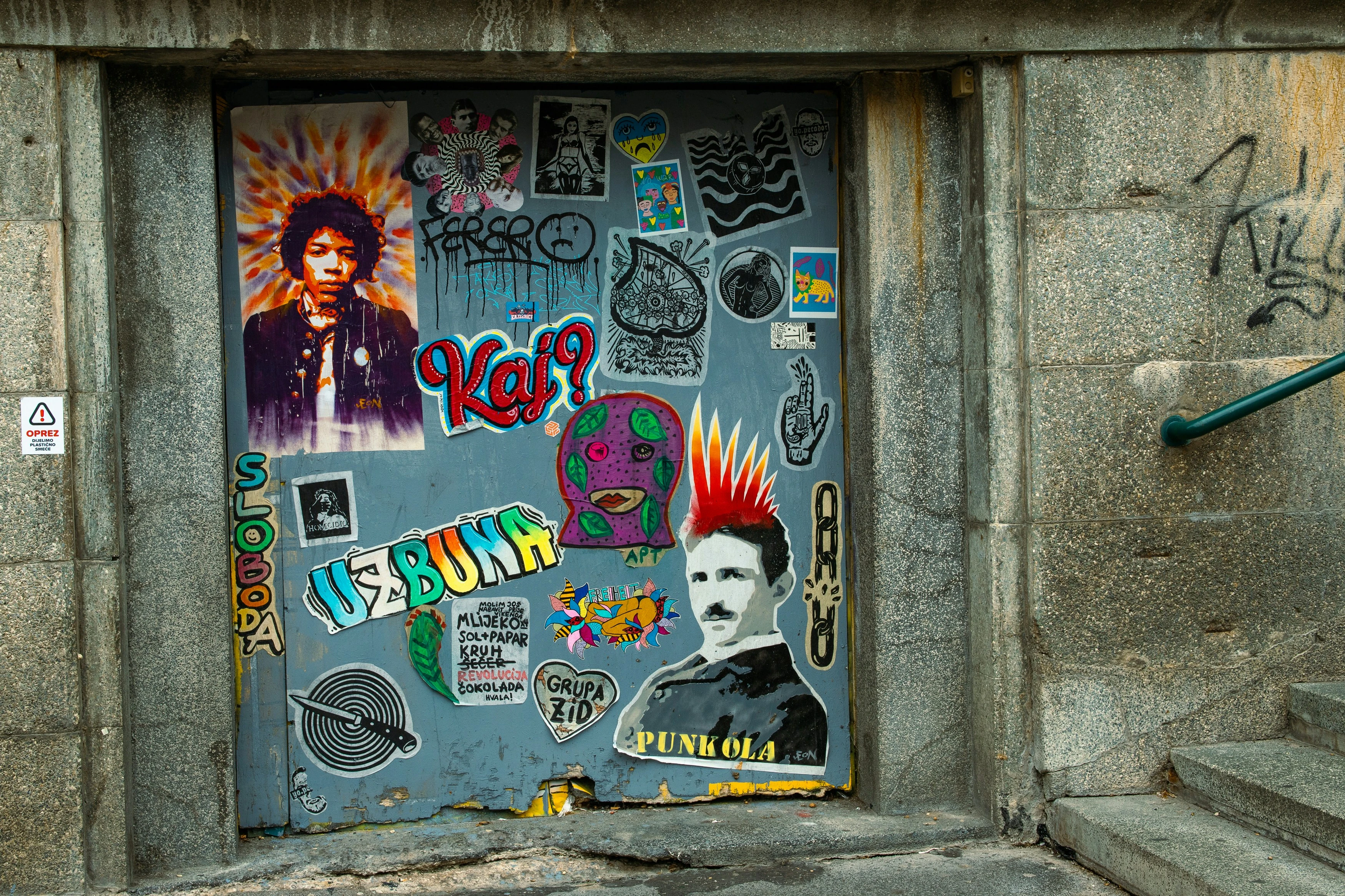 Blue door covered in colorful stickers and street art on concrete wall steps.
