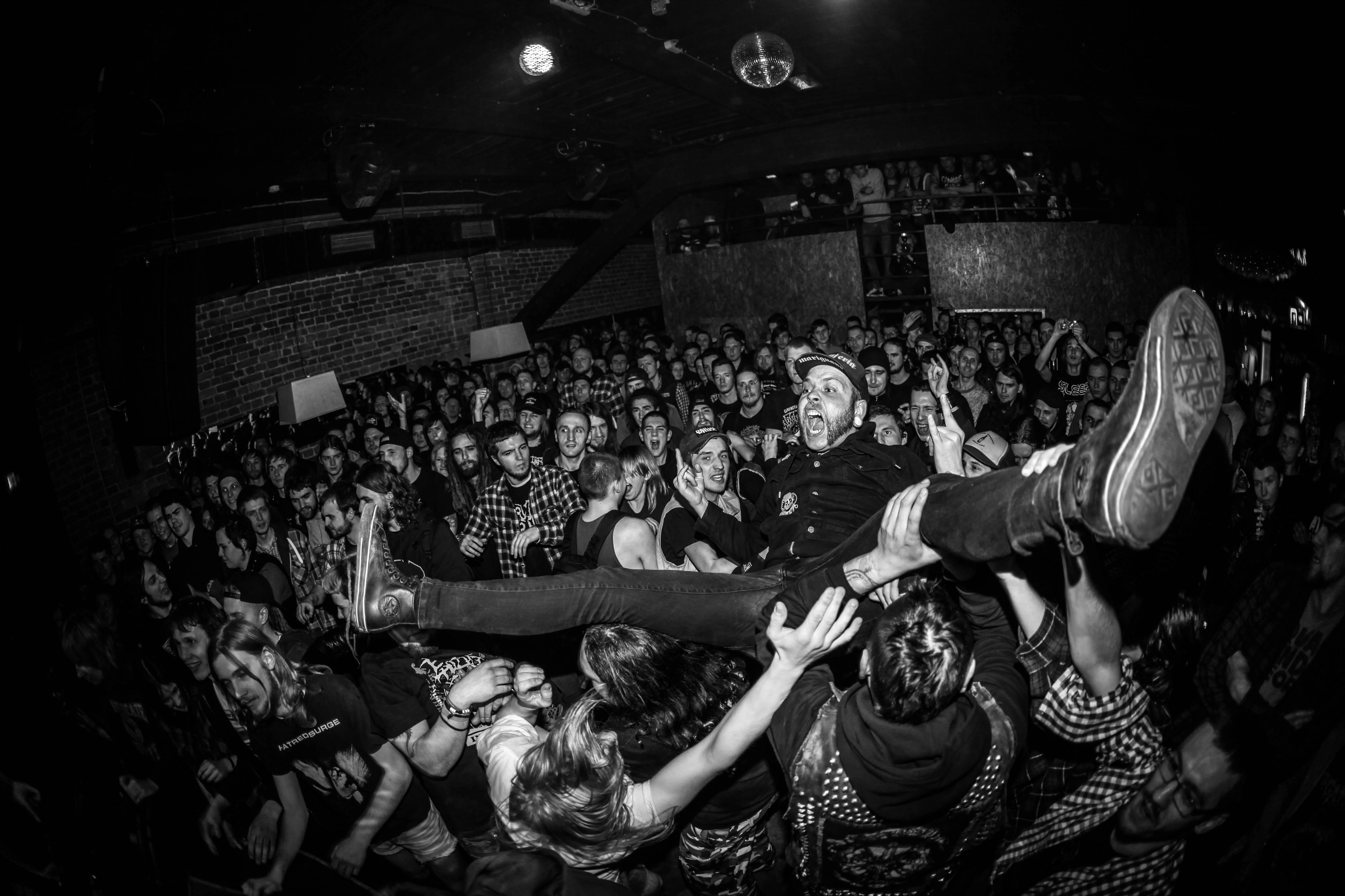 Black and white concert photo showing crowd surfing performer above packed audience.