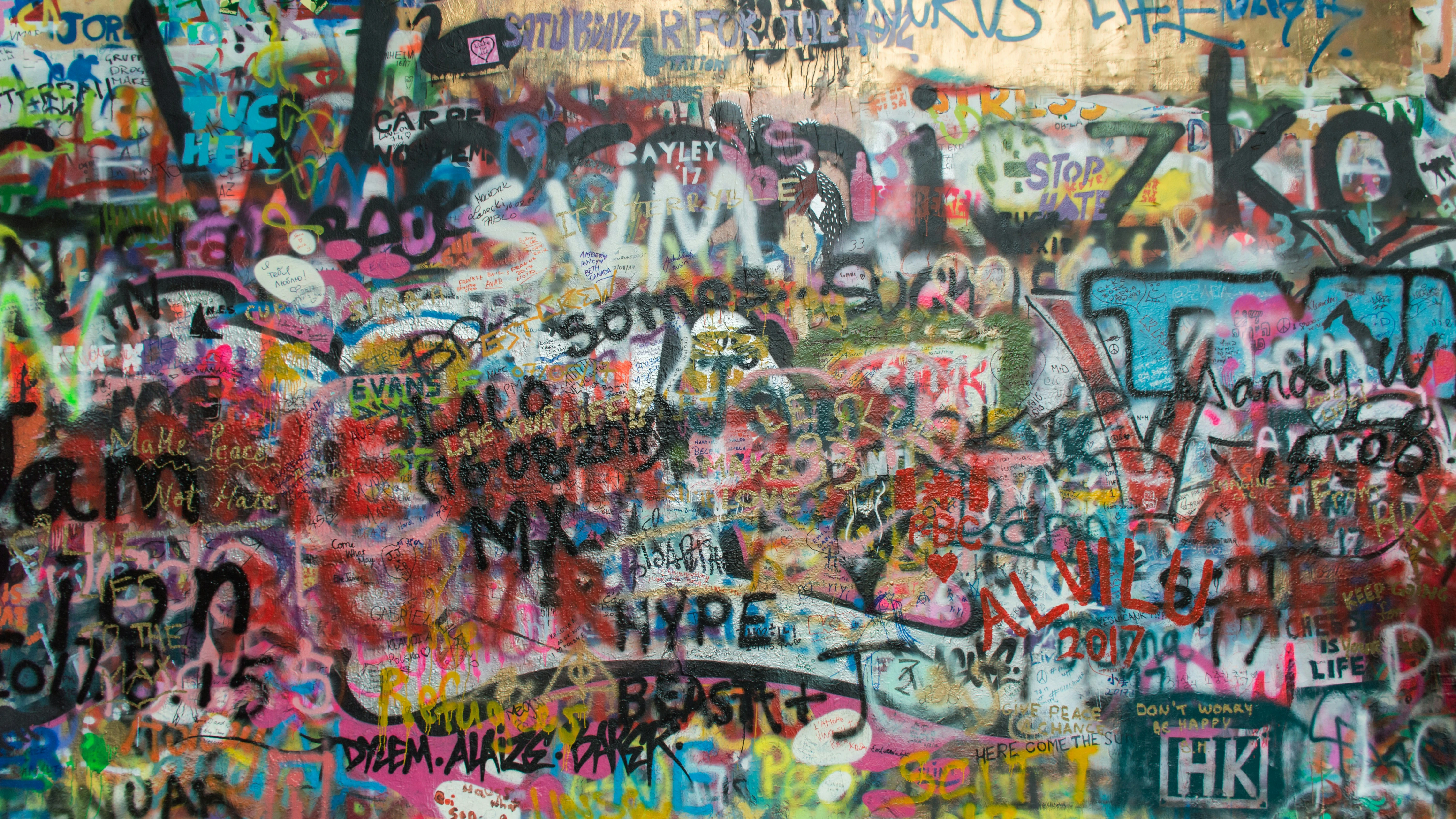 Colorful graffiti wall covered in layered spray paint tags, stickers and street art.